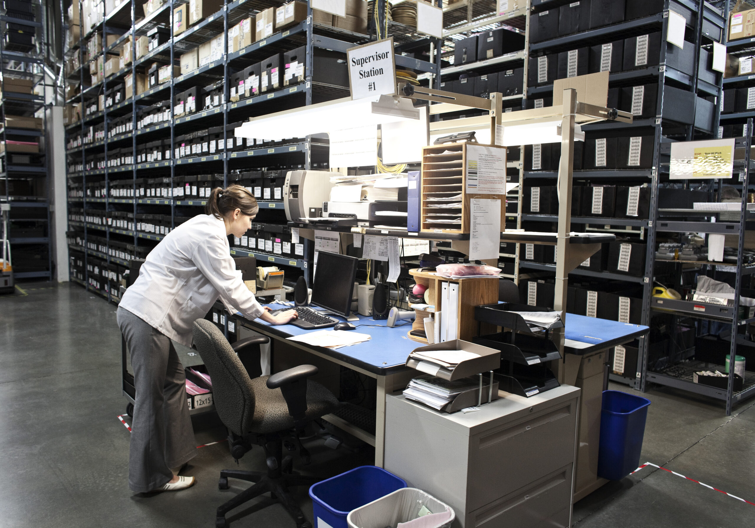 Document Processing - Logistics employee manually processing shipment documents in a warehouse office, illustrating document-heavy cargo operations and administrative workload.